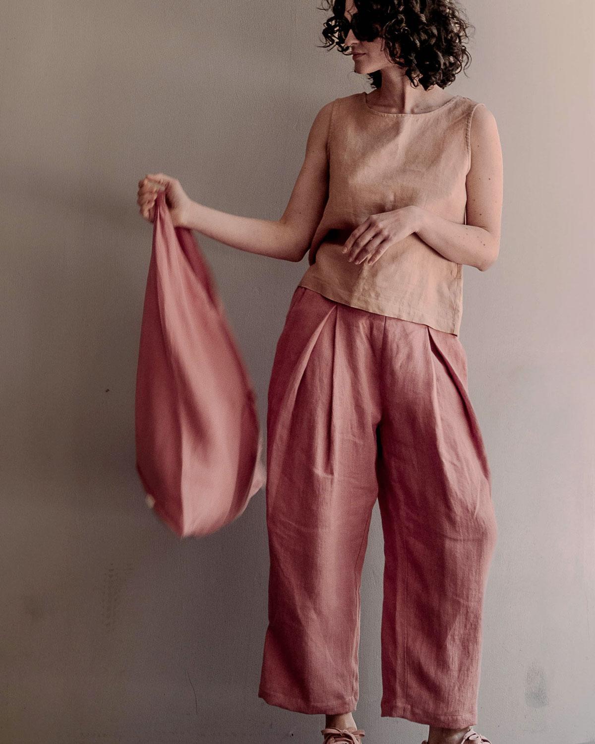 Kobieta w szerokich różowych spodniach lnianych z wysokim stanem i lnianym topie trzymająca materiałową torbę.